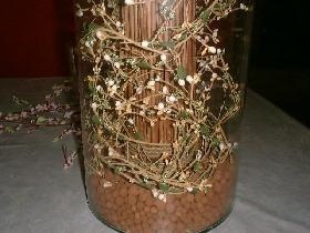 placer la botte de branches ( sans enlever le lien à la base ) dans le vase en la tassant dans les billes pour la maintenir droite <p>entourer la base de la botte avec la guirlande fleurie